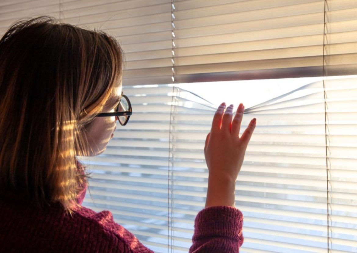 Une personne ajuste des lamelles de volets et stores roulants pour regarder à travers.