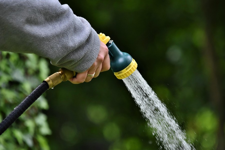 Une main tenant un pistolet d'arrosage dans un jardin pour montrer qu'il est possible de réduire sa consommation d'eau de 90% avec une douche à circuit fermé dans le reste de la maison.