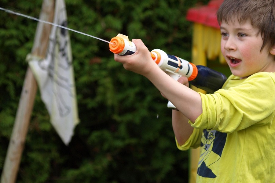 Un jeune garçon concentré projetant un jet d'eau précis, un exercice de dextérité rappelant la minutie nécessaire pour savoir comment régler son pistolet à peinture pour un fini laqué sans peau d'orange.