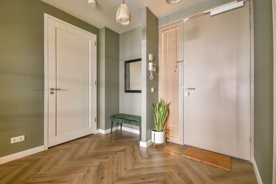 Une entrée étroite bien aménagée avec des murs vert sauge, un parquet en chevrons, un miroir noir et un banc vert.