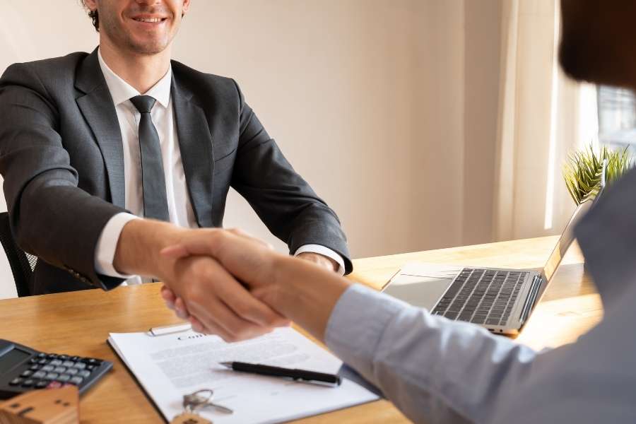 Un homme en costume serre la main d'un client lors d'un rendez-vous professionnel axé sur la gestion locative privée.