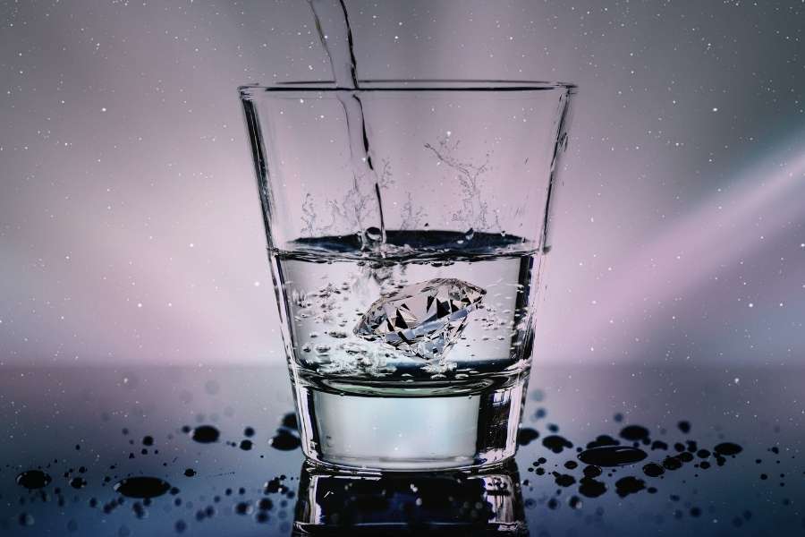 Un filet d'eau dynamisée versé dans un verre transparent contenant un diamant étincelant.