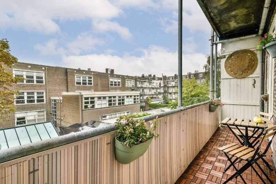 Un petit balcon urbain avec un sol en caillebotis de bois et une balustrade en bois claire, où l'on voit comment végétaliser un mur de balcon à l'aide de jardinières suspendues.